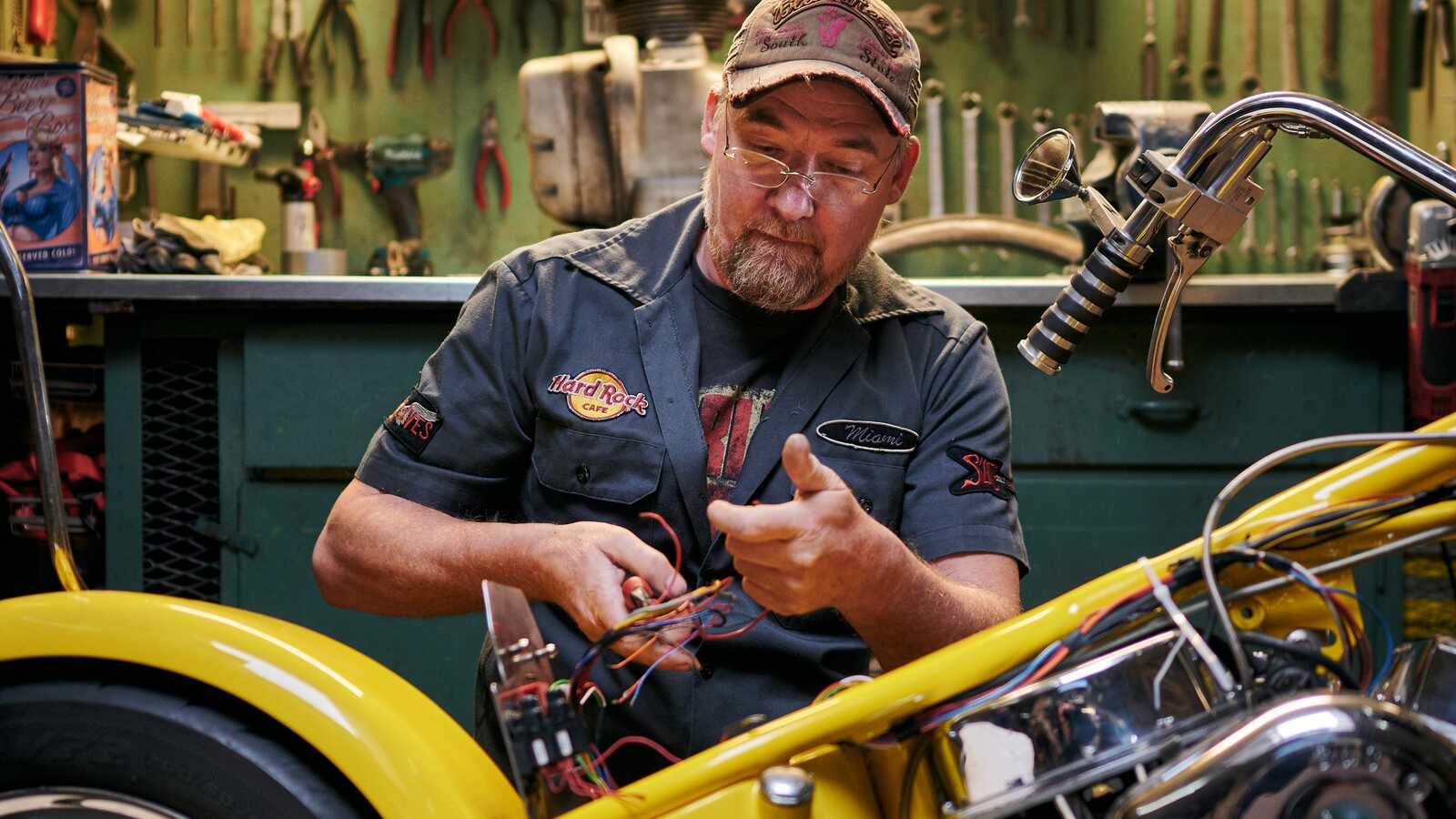 Ein Mann repariert ein Motorad, im Hintergrund befindet sich eine Werkbank und Werkzeug.